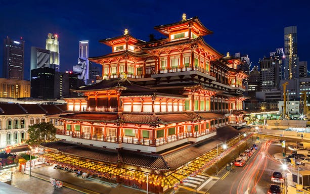 Chinese temple illuminated at night in Singapore's Chinatown with city skyline.