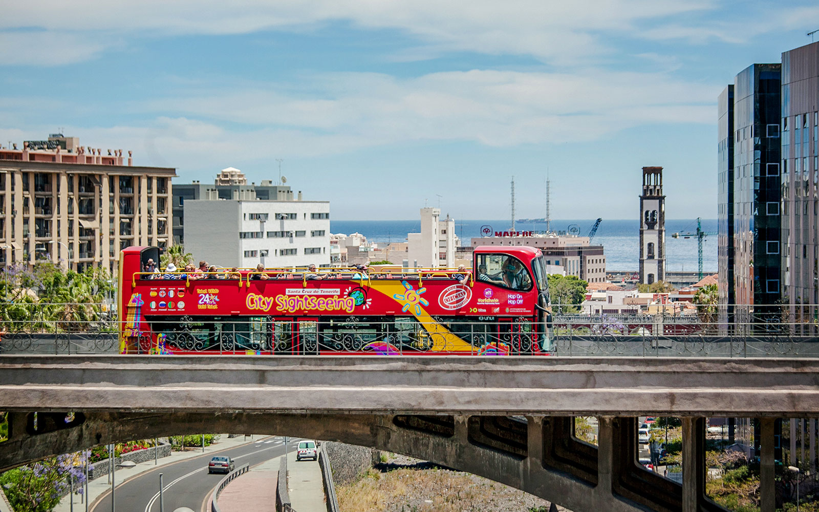 Open-top sightseeing bus in Santa Cruz with cityscape and ocean in the background.