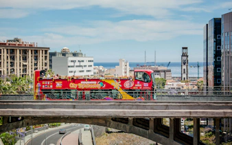 Open-top sightseeing bus in Santa Cruz with cityscape and ocean in the background.