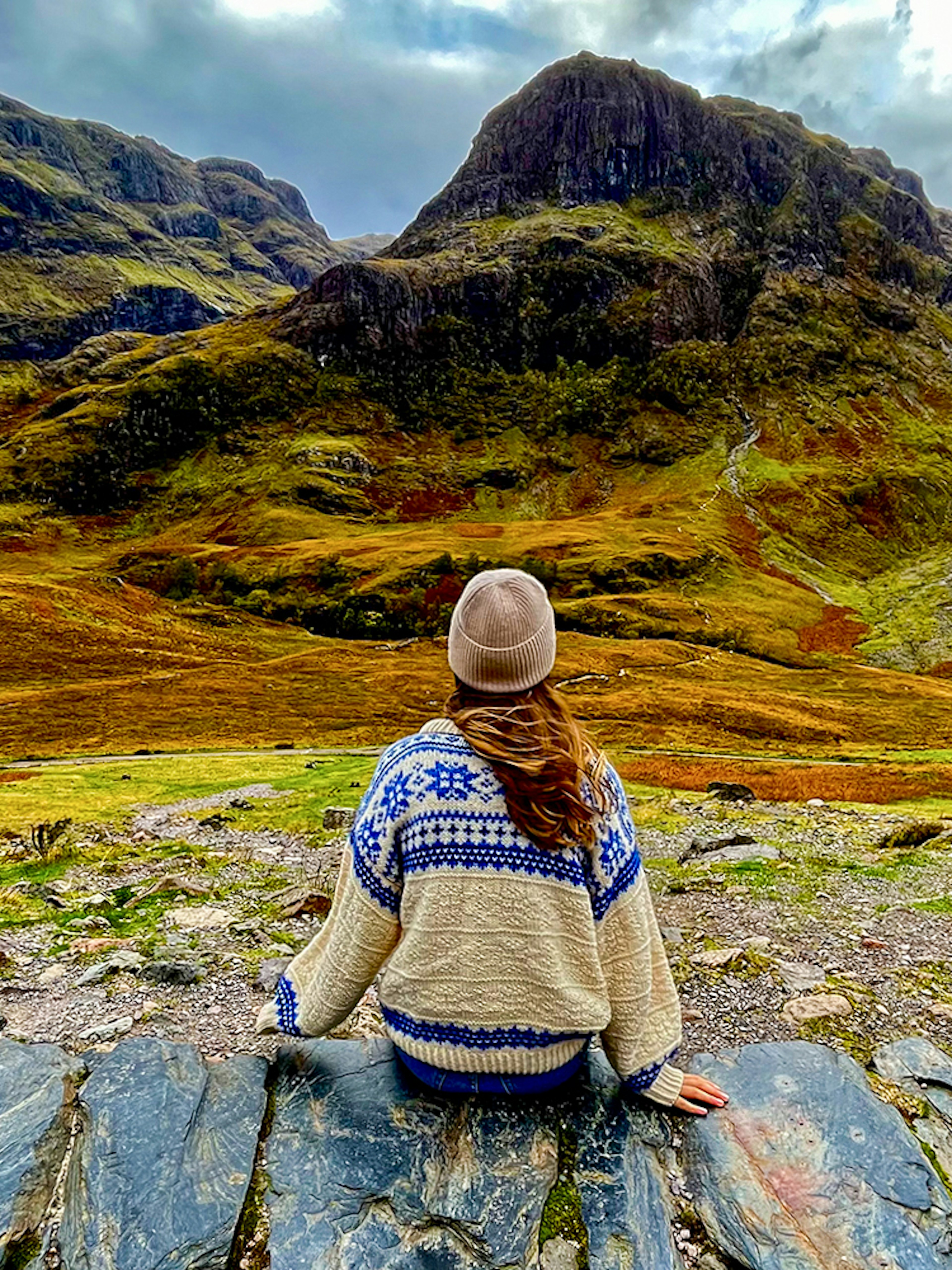 Person sitting on rocks overlooking the Highlands landscape near Loch Ness on an Edinburgh day trip.