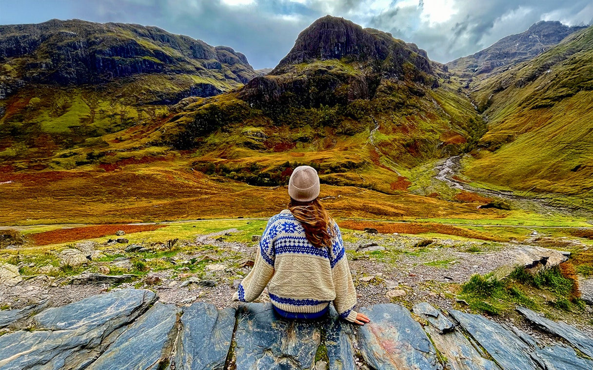 Person sitting on rocks overlooking the Highlands landscape near Loch Ness on an Edinburgh day trip.