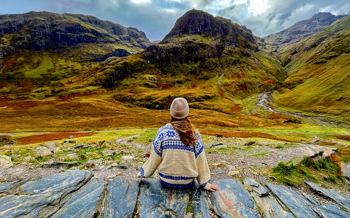 Person sitting on rocks overlooking the Highlands landscape near Loch Ness on an Edinburgh day trip.