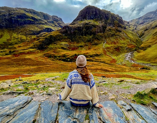 Person sitting on rocks overlooking the Highlands landscape near Loch Ness on an Edinburgh day trip.