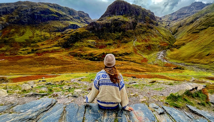 Person sitting on rocks overlooking the Highlands landscape near Loch Ness on an Edinburgh day trip.