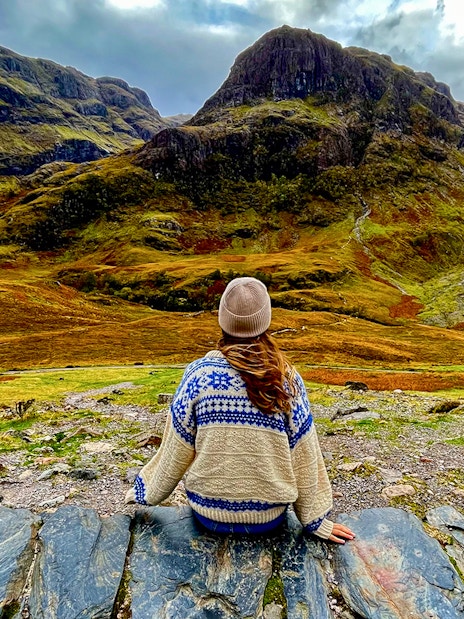 Person sitting on rocks overlooking the Highlands landscape near Loch Ness on an Edinburgh day trip.
