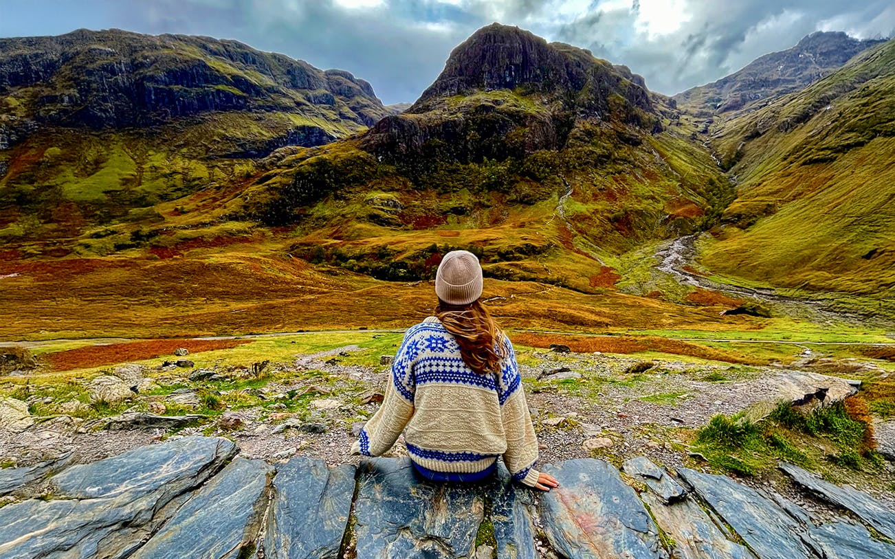 Person sitting on rocks overlooking the Highlands landscape near Loch Ness on an Edinburgh day trip.
