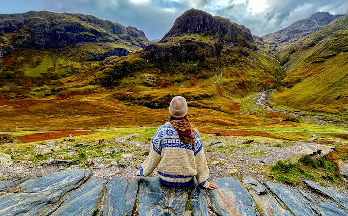 Person sitting on rocks overlooking the Highlands landscape near Loch Ness on an Edinburgh day trip.