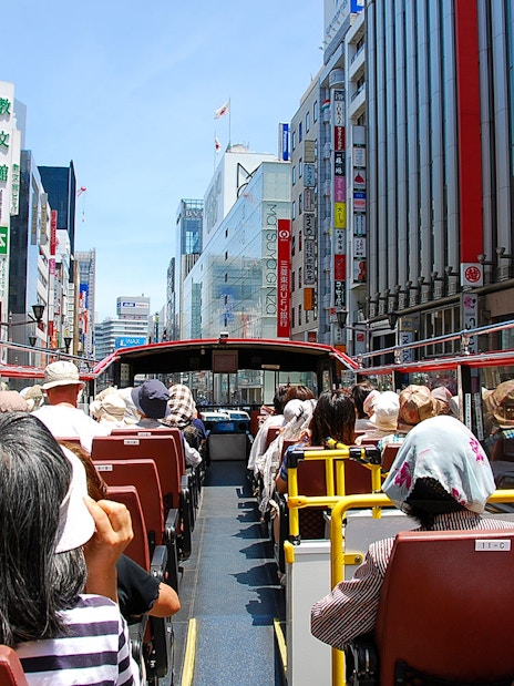 Tourists on a Sky Hop Bus tour in Tokyo, Japan, viewing city buildings and signs.