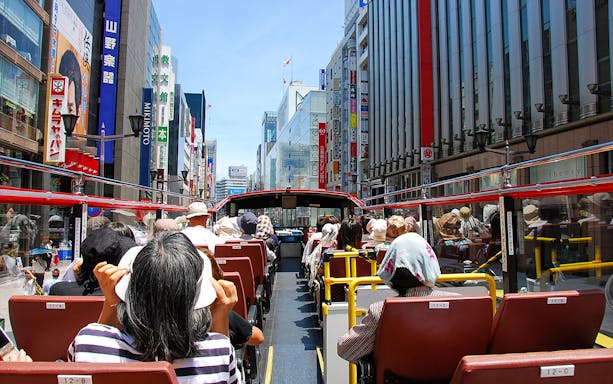 Tourists on a Sky Hop Bus tour in Tokyo, Japan, viewing city buildings and signs.