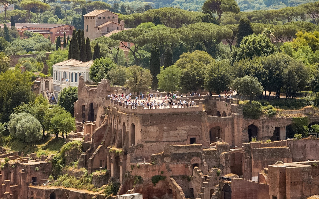 Tourists exploring Palatine Hill ruins in Rome, surrounded by lush greenery.
