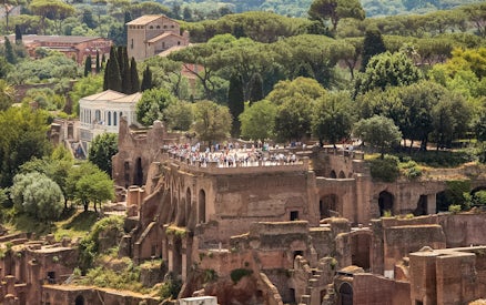 Tourists exploring Palatine Hill ruins in Rome, surrounded by lush greenery.
