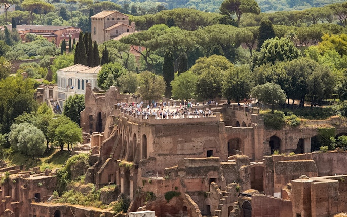 Tourists exploring Palatine Hill ruins in Rome, surrounded by lush greenery.