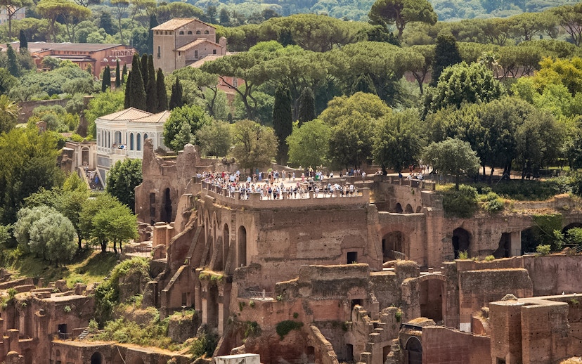 Tourists exploring Palatine Hill ruins in Rome, surrounded by lush greenery.