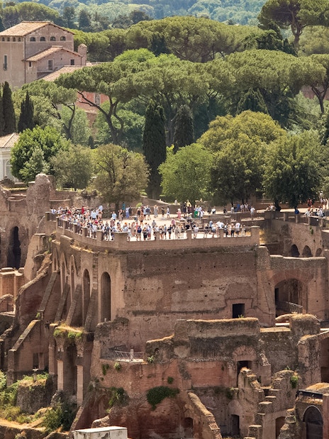Tourists exploring Palatine Hill ruins in Rome, surrounded by lush greenery.