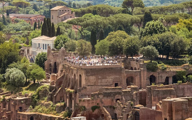 Tourists exploring Palatine Hill ruins in Rome, surrounded by lush greenery.