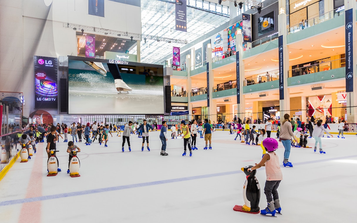 People ice skating at Dubai Ice Rink inside a bustling shopping mall.