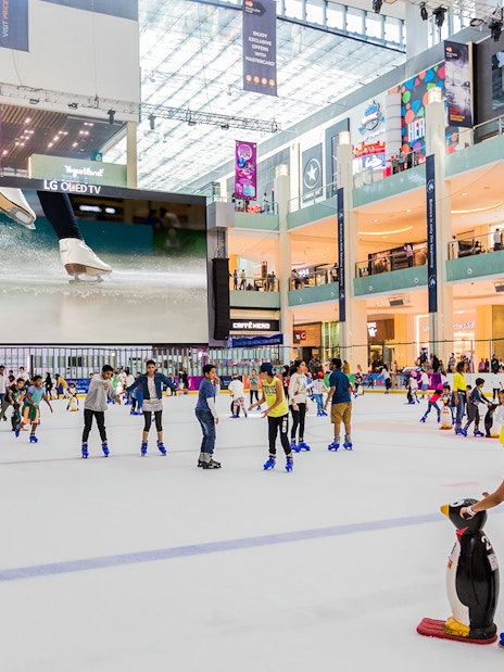 People ice skating at Dubai Ice Rink inside a bustling shopping mall.