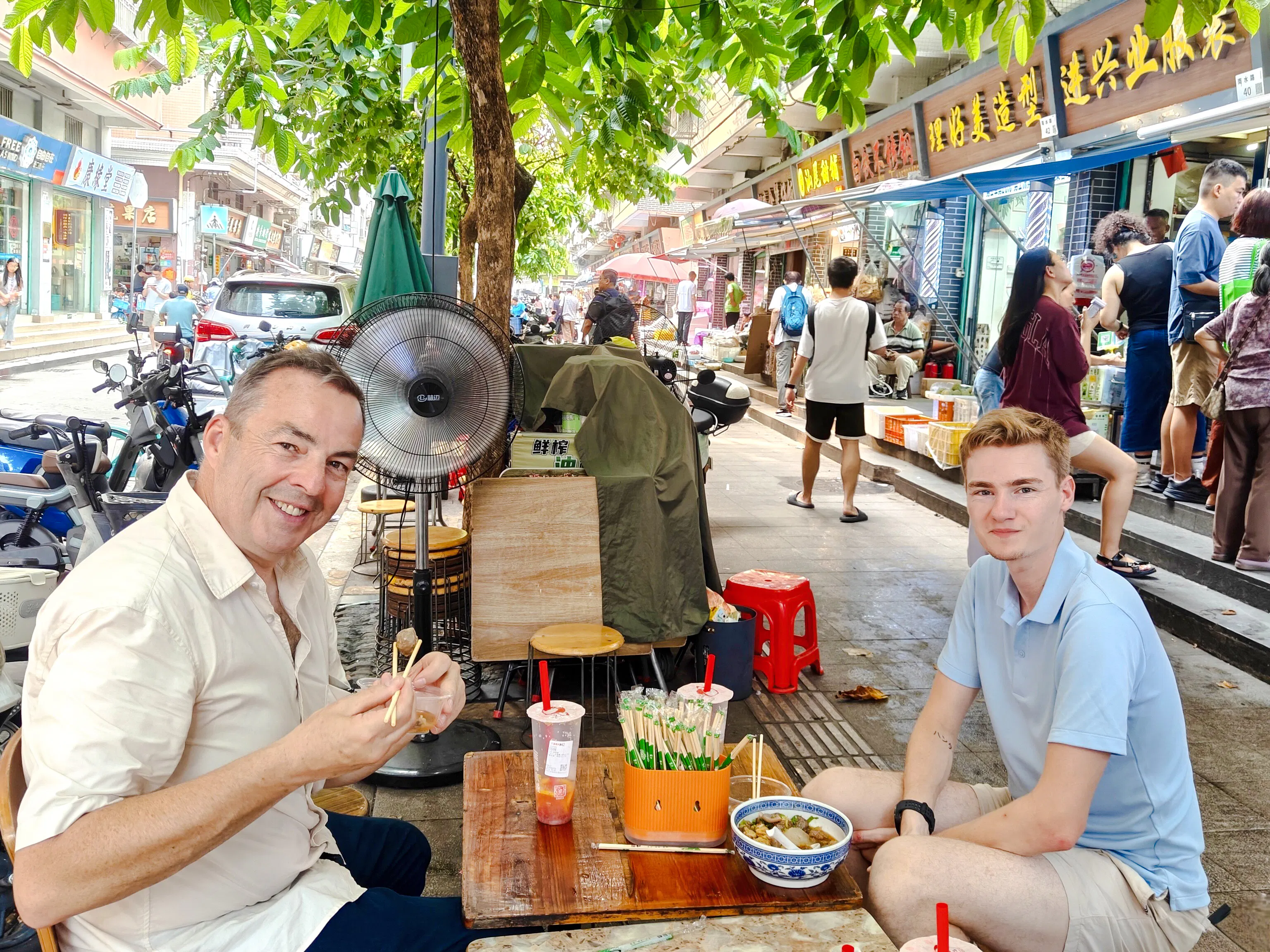 Street dining in Shenzhen local neighborhood, people enjoying food and vibrant atmosphere.