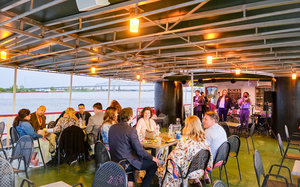 People dining on Steamboat Natchez with live band and river view in New Orleans.
