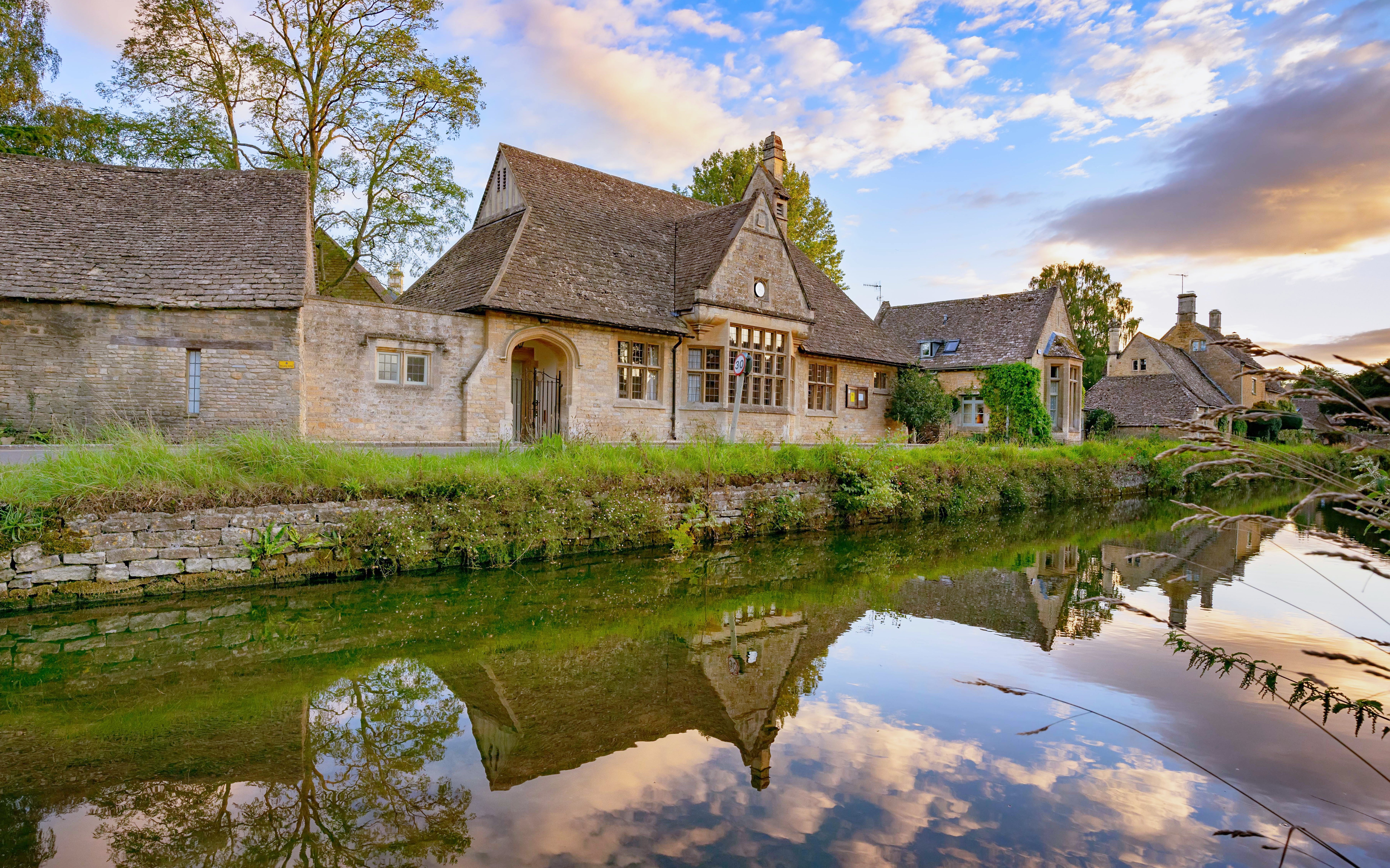 Stone cottages reflected in a tranquil river in the Cotswolds, England.