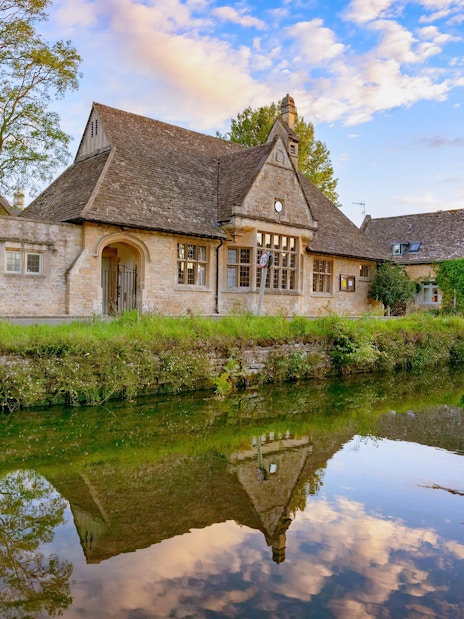 Stone cottages reflected in a tranquil river in the Cotswolds, England.