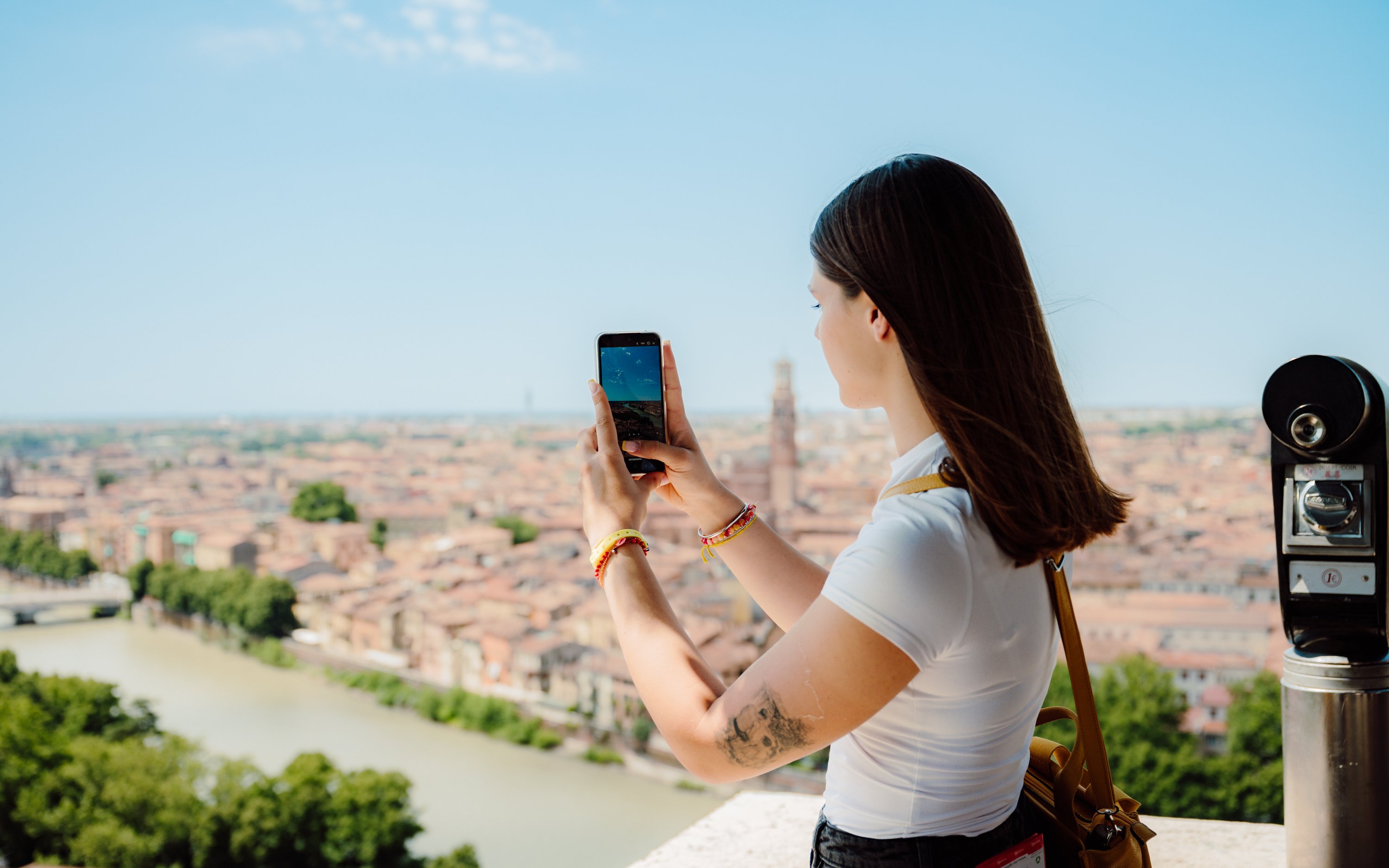 Tourist photographing Verona cityscape from a viewpoint during hop-on hop-off bus tour.