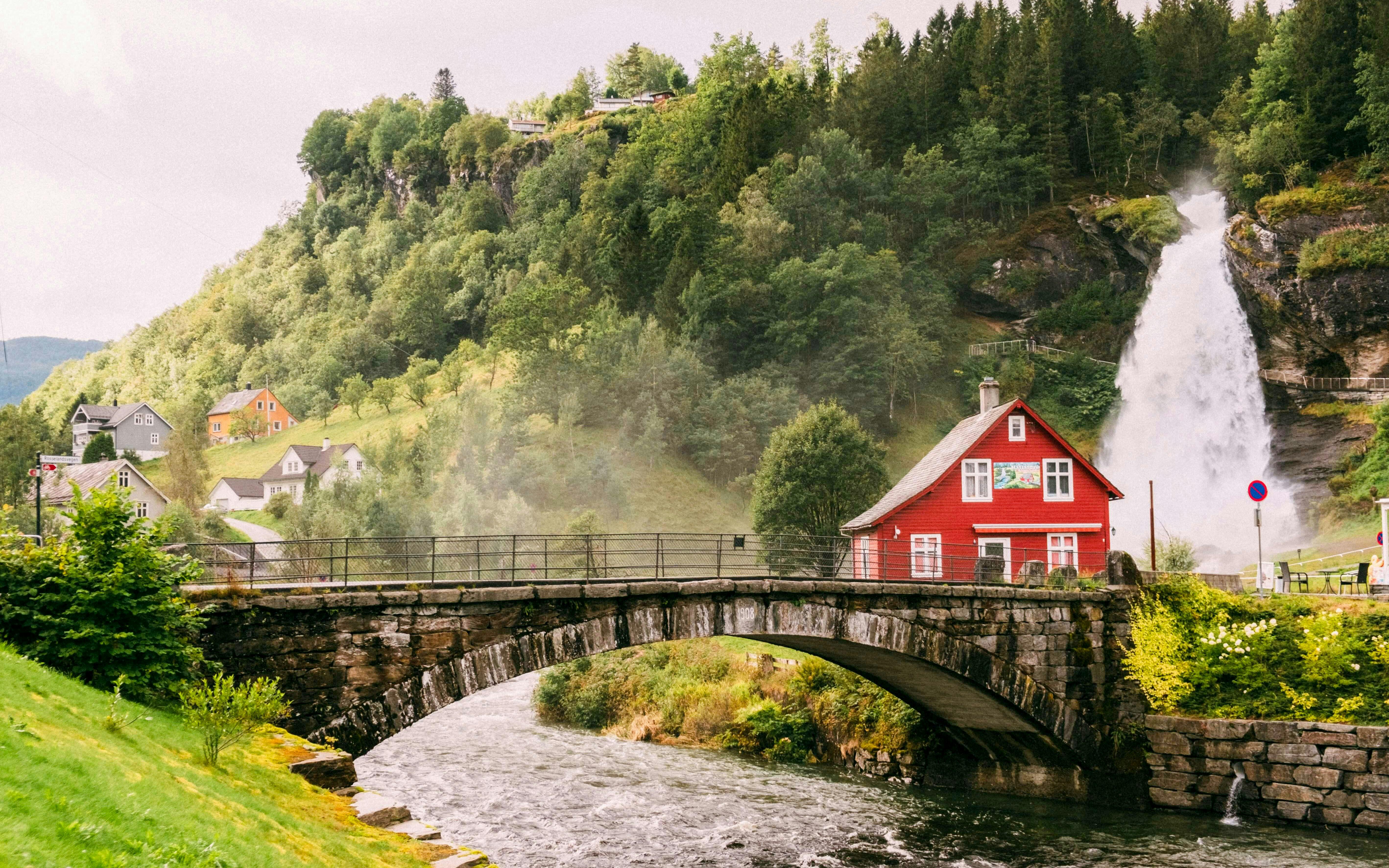 Steinsdalsfossen Waterfall with red house and bridge, Folgefonna National Park, Norway.