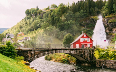 Steinsdalsfossen Waterfall with red house and bridge, Folgefonna National Park, Norway.