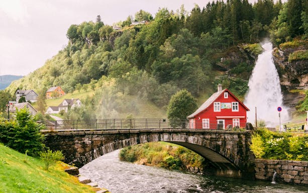 Steinsdalsfossen Waterfall with red house and bridge, Folgefonna National Park, Norway.