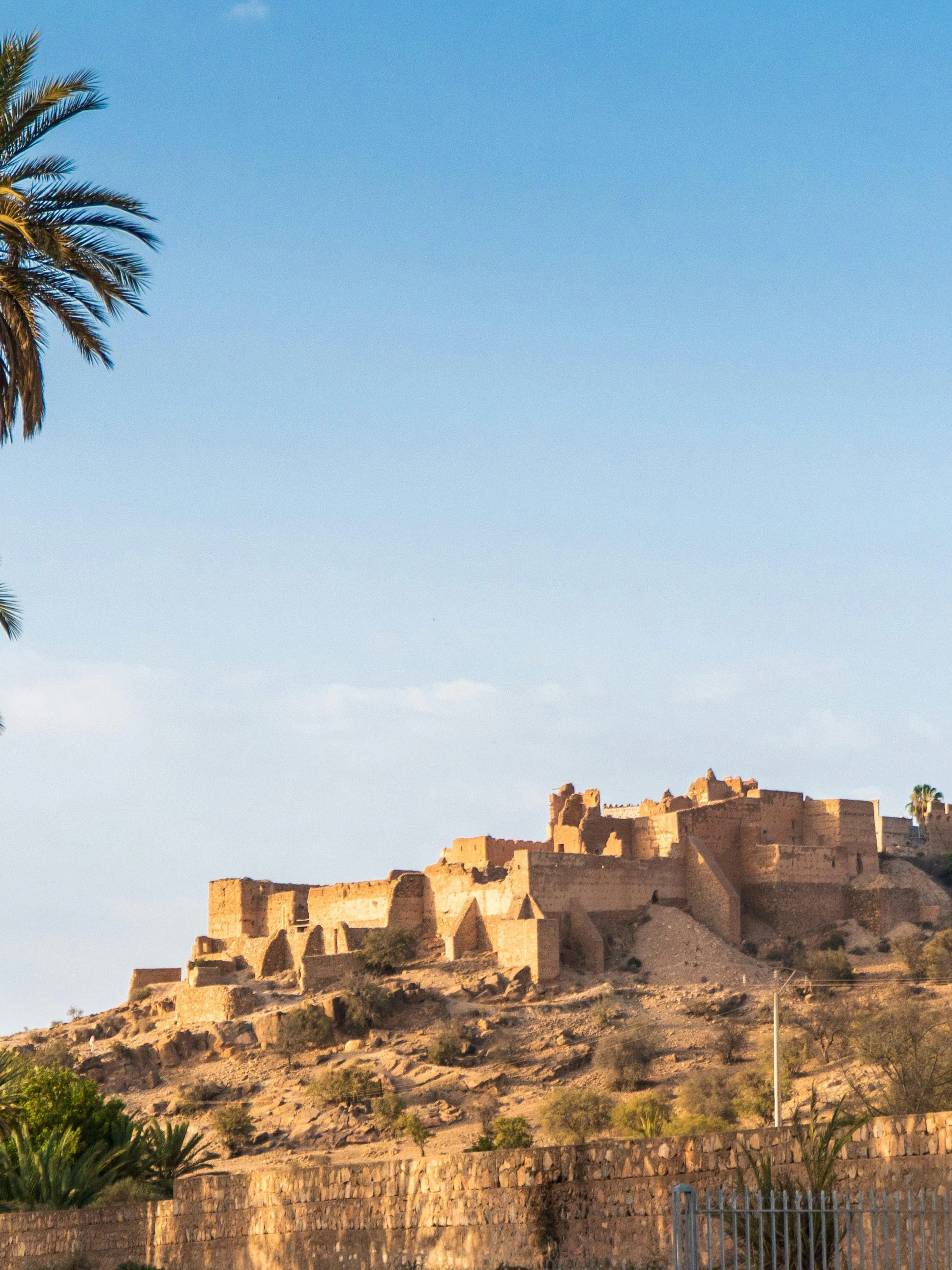 Tiout village with historical mountain and palm trees under clear blue sky, Taroudant, Morocco.