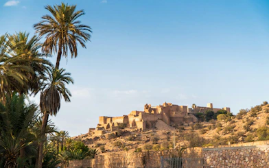 Tiout village with historical mountain and palm trees under clear blue sky, Taroudant, Morocco.