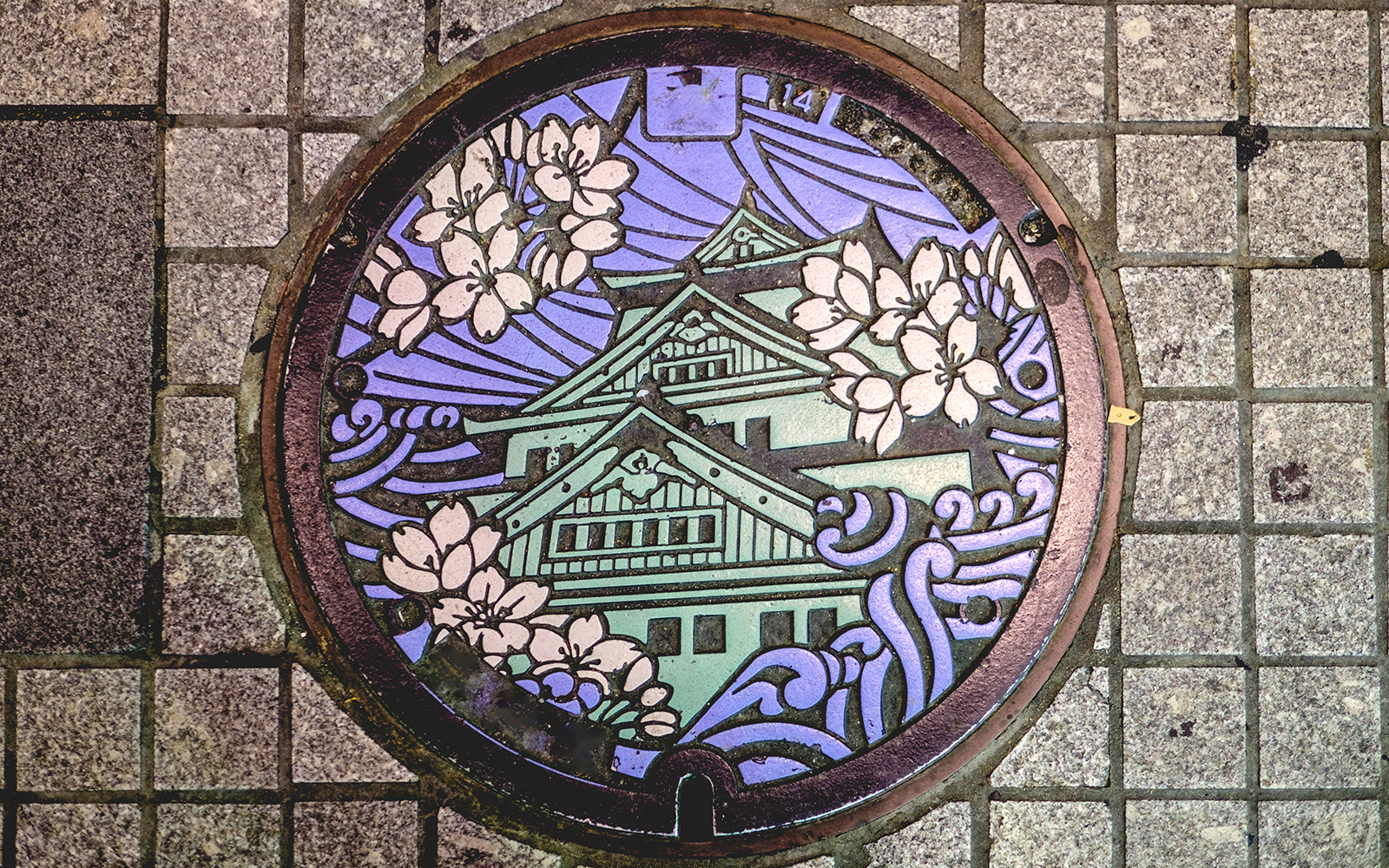 Decorative manhole cover featuring Osaka Castle and cherry blossoms in Osaka Namba.