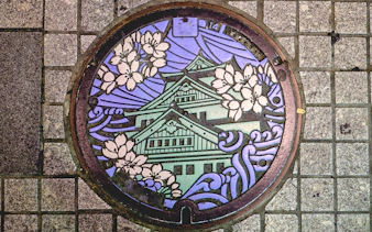 Decorative manhole cover featuring Osaka Castle and cherry blossoms in Osaka Namba.