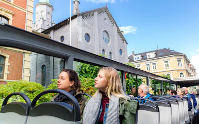 Tourists on Bergen Hop on Hop off bus passing historic buildings.