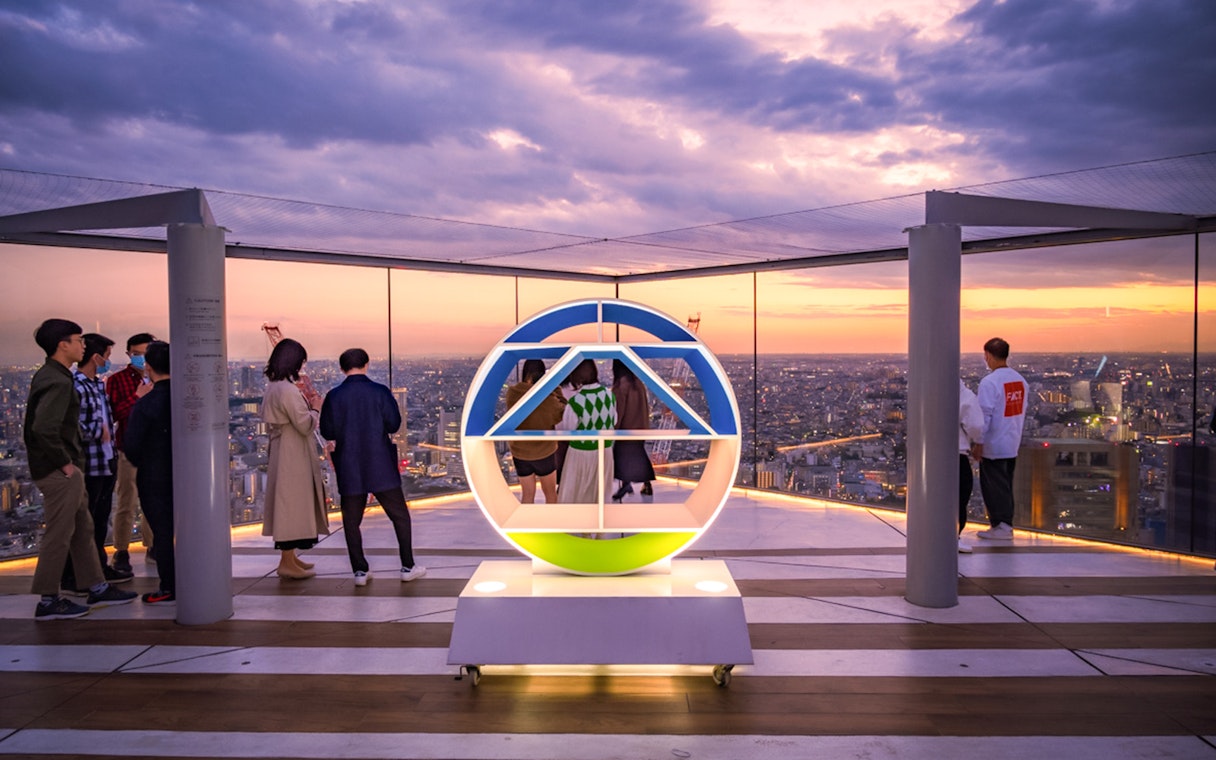 Tourists enjoying sunset views from Shibuya Sky Deck in Tokyo.