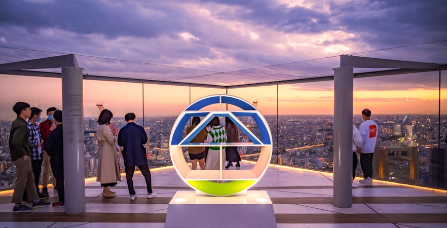 Tourists enjoying sunset views from Shibuya Sky Deck in Tokyo.