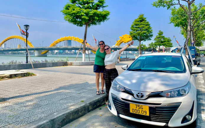 Friends posing by car near Dragon Bridge, Da Nang, on Hue to Hoi An tour via Hai Van Pass.