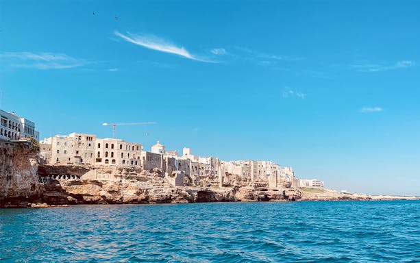 Polignano a Mare coastline viewed from a boat tour with caves and historic buildings.