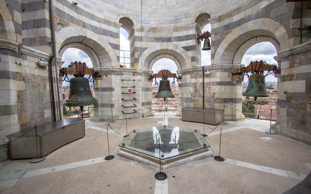 Bells inside the tower of Pisa, Italy, with city view through arches.