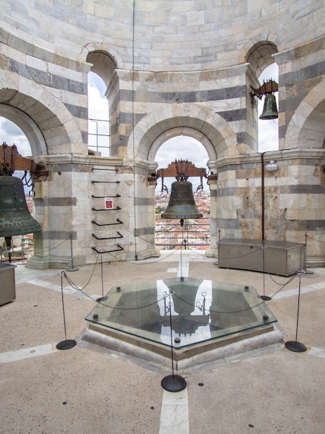 Bells inside the tower of Pisa, Italy, with city view through arches.