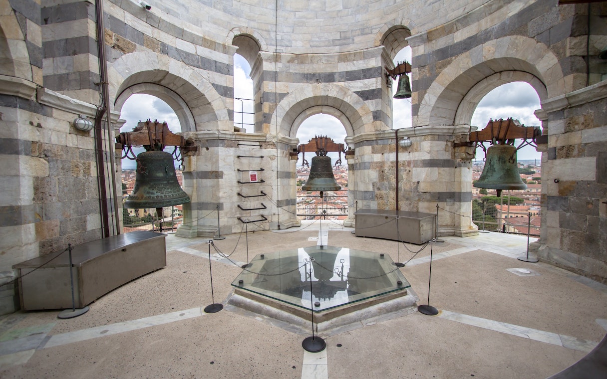Bells inside the tower of Pisa, Italy, with city view through arches.