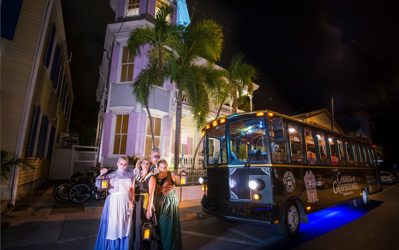 Ghosts & Gravestones tour trolley at night with costumed guides in front of a historic house.