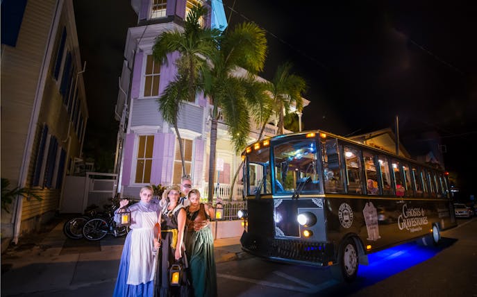 Ghosts & Gravestones tour trolley at night with costumed guides in front of a historic house.