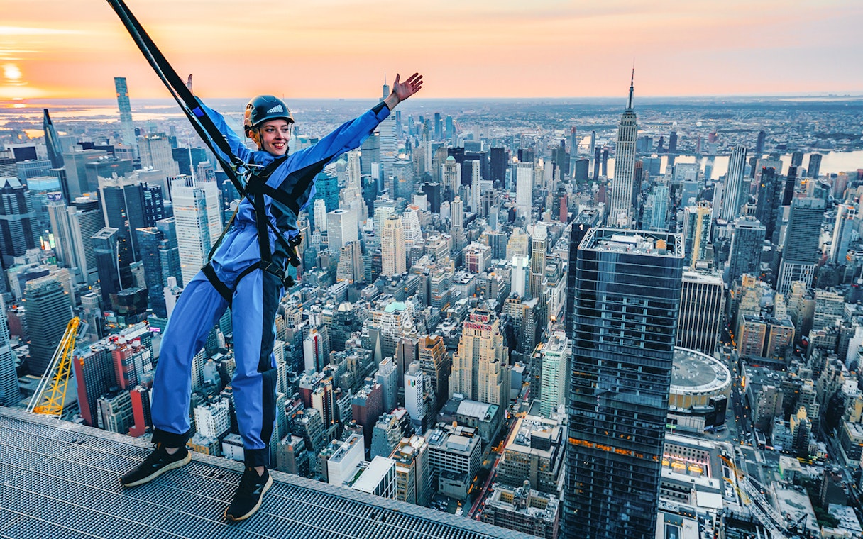 Person harnessed on skyscraper edge with New York City skyline in background during City Climb Experience.