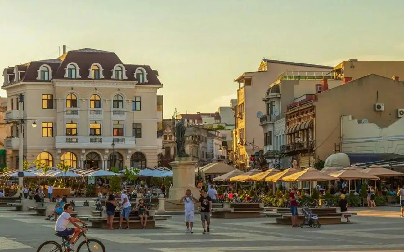 Constanța Old Town square with people, historic buildings, and outdoor cafes at sunset.