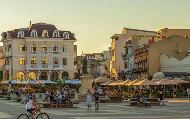 Constanța Old Town square with people, historic buildings, and outdoor cafes at sunset.