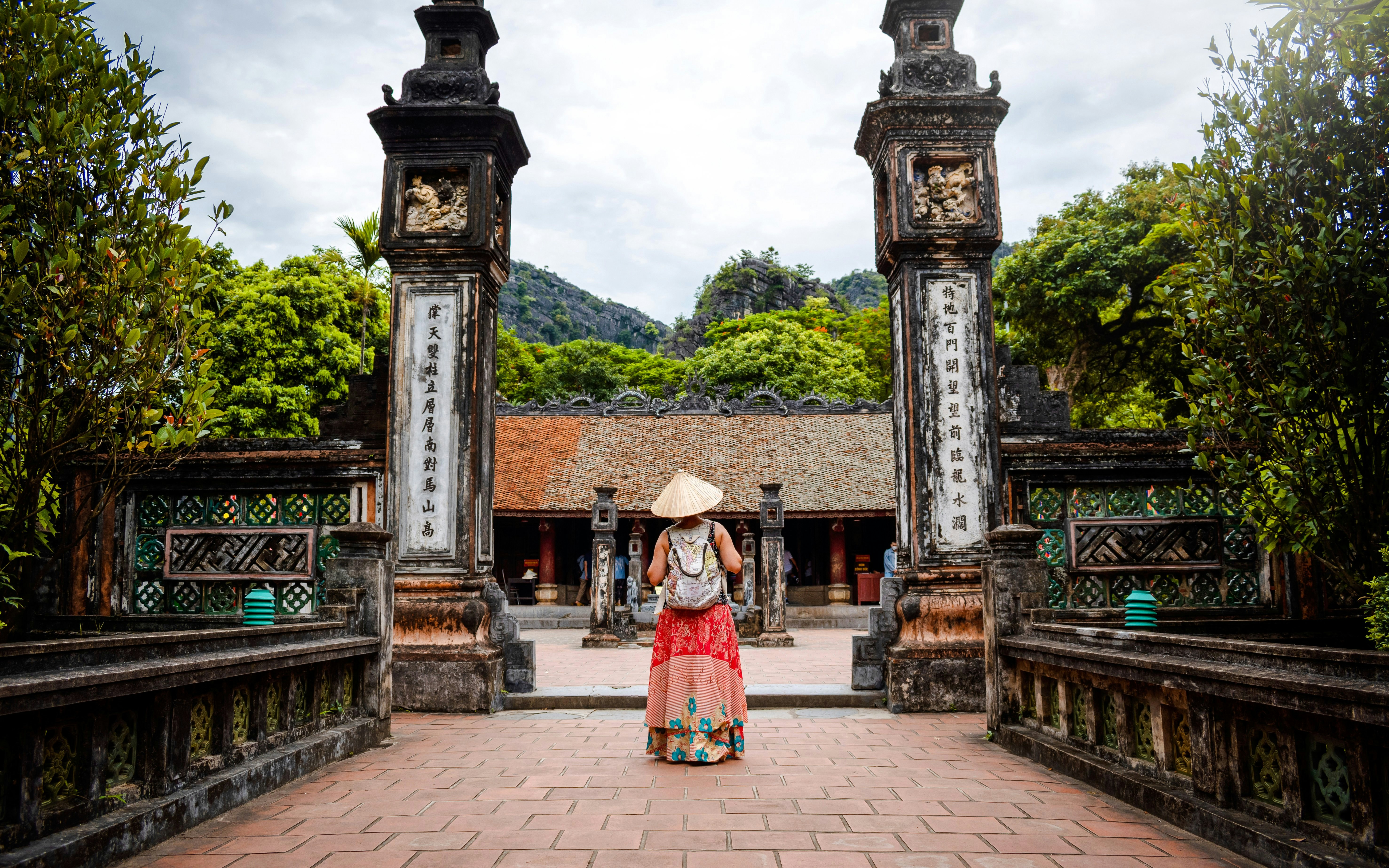 Tourist in traditional hat exploring ancient gate at Hoa Lu, Vietnam.