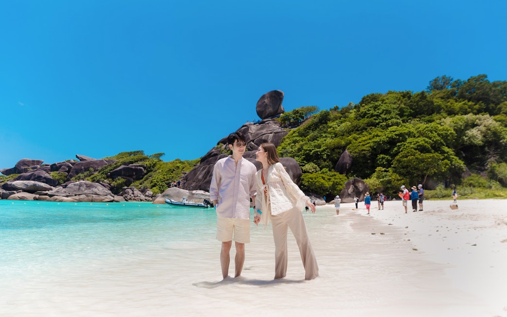 Tourists enjoying the beach on Similan Island, Thailand, with clear water and rocky backdrop.
