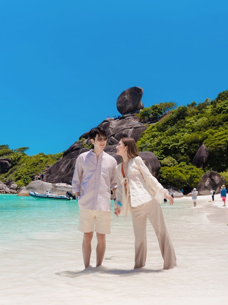 Tourists enjoying the beach on Similan Island, Thailand, with clear water and rocky backdrop.