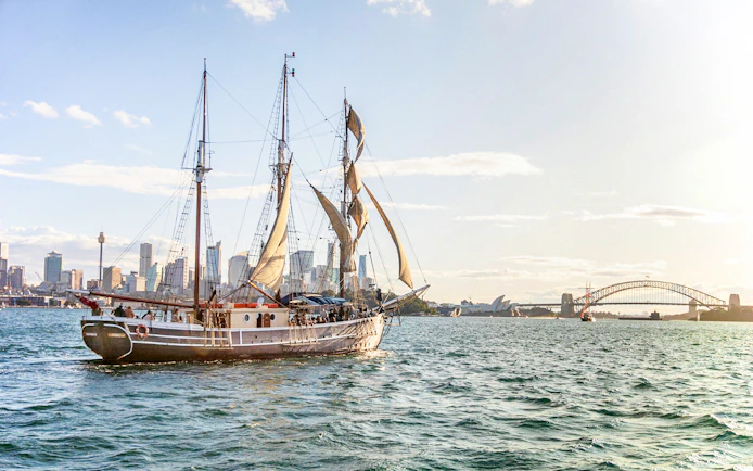 Tall ship sailing in Sydney Harbour with Harbour Bridge in the background.